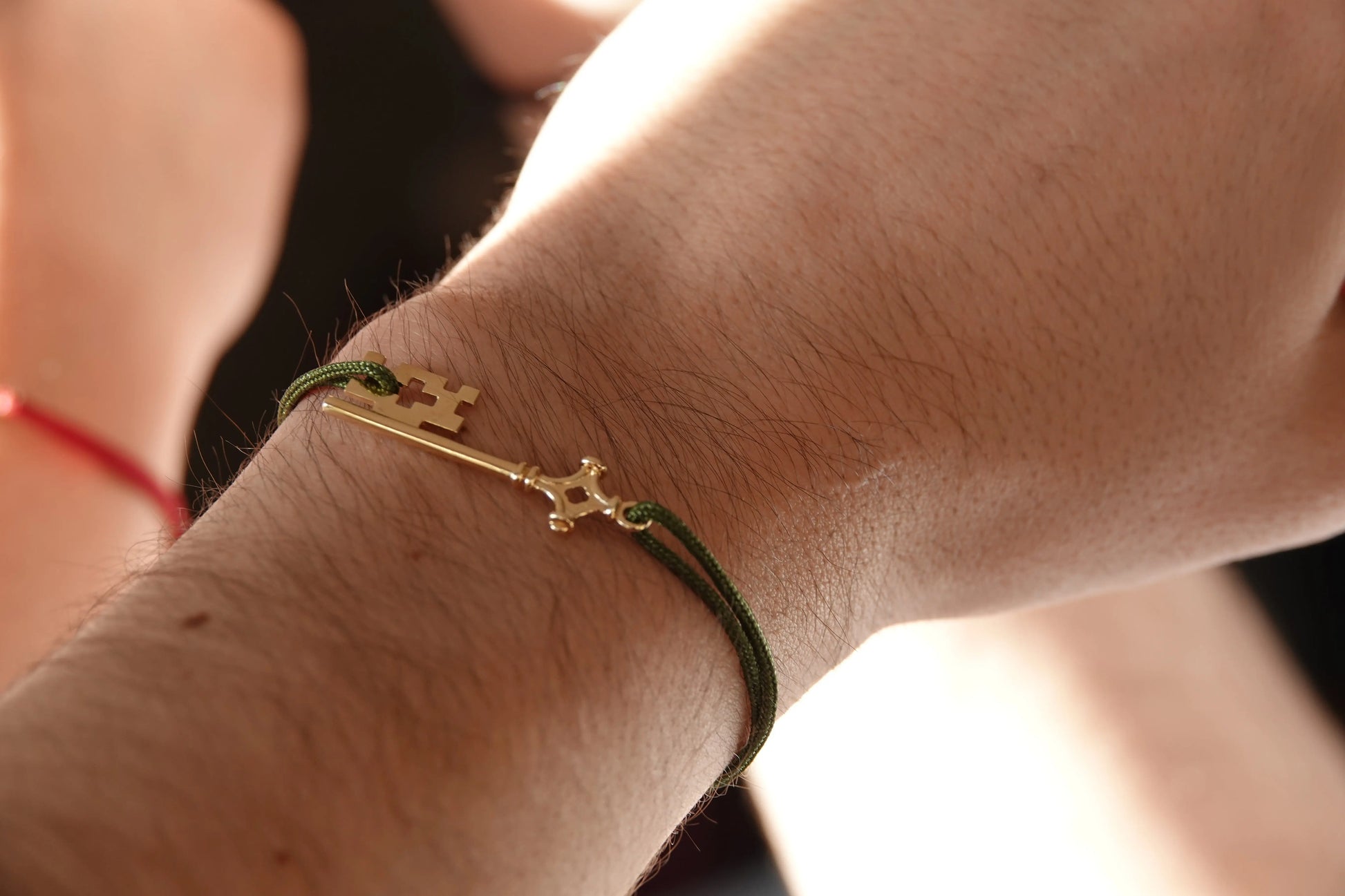 Bracelet GenevaKey en argent plaqué or jaune et cordon vert sur le poignet d'un homme