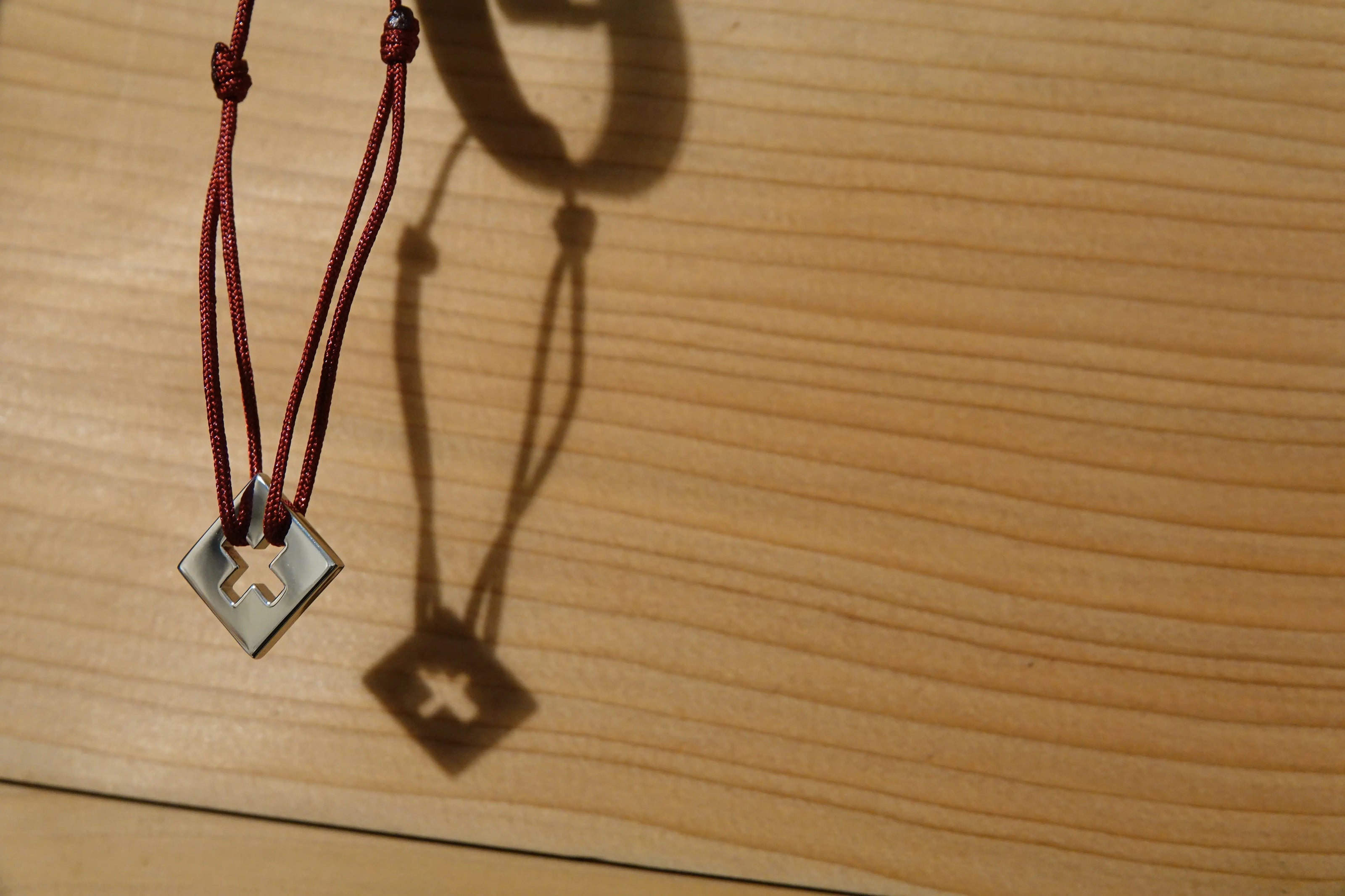 Bracelet SwissFlag en argent rhodié et cordon rouge pendu sur un crochet contre un mur en bois