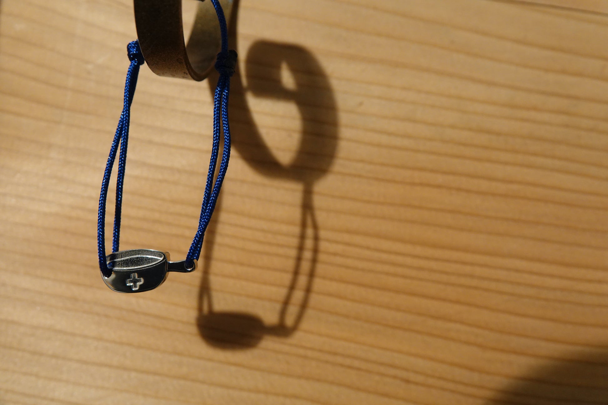 Bracelet SwissFondue en argent rhodié et cordon bleu suspendu sur un crochet contre un mur en bois