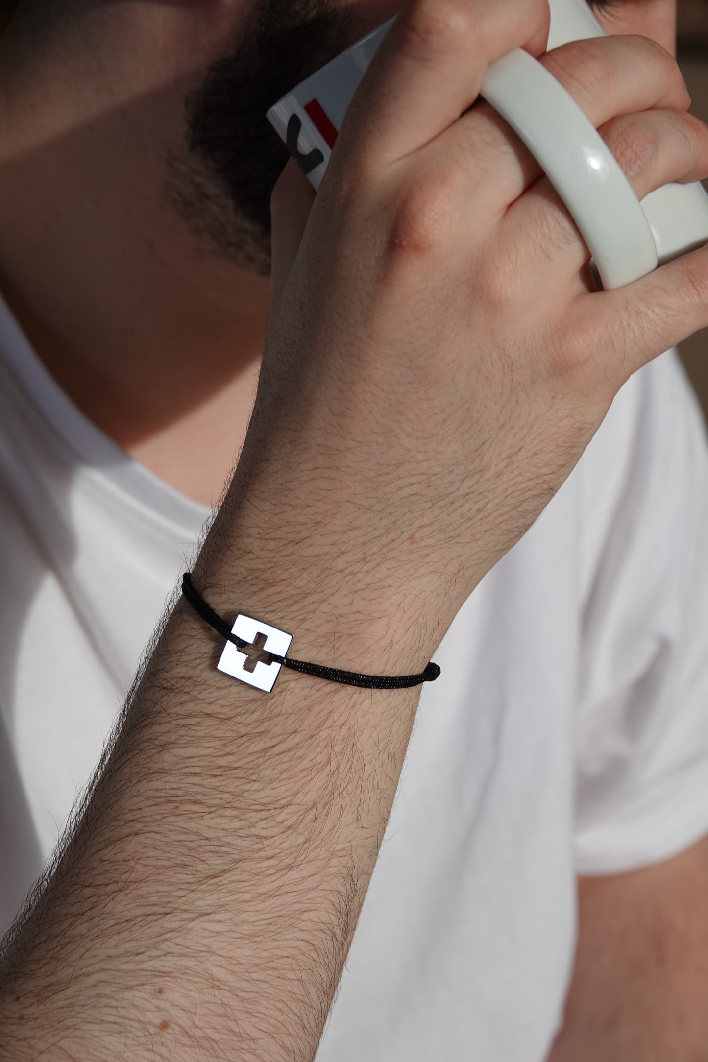 Bracelet SwissFlag en argent rhodié et cordon noir sur poignet d'homme qui boit un café