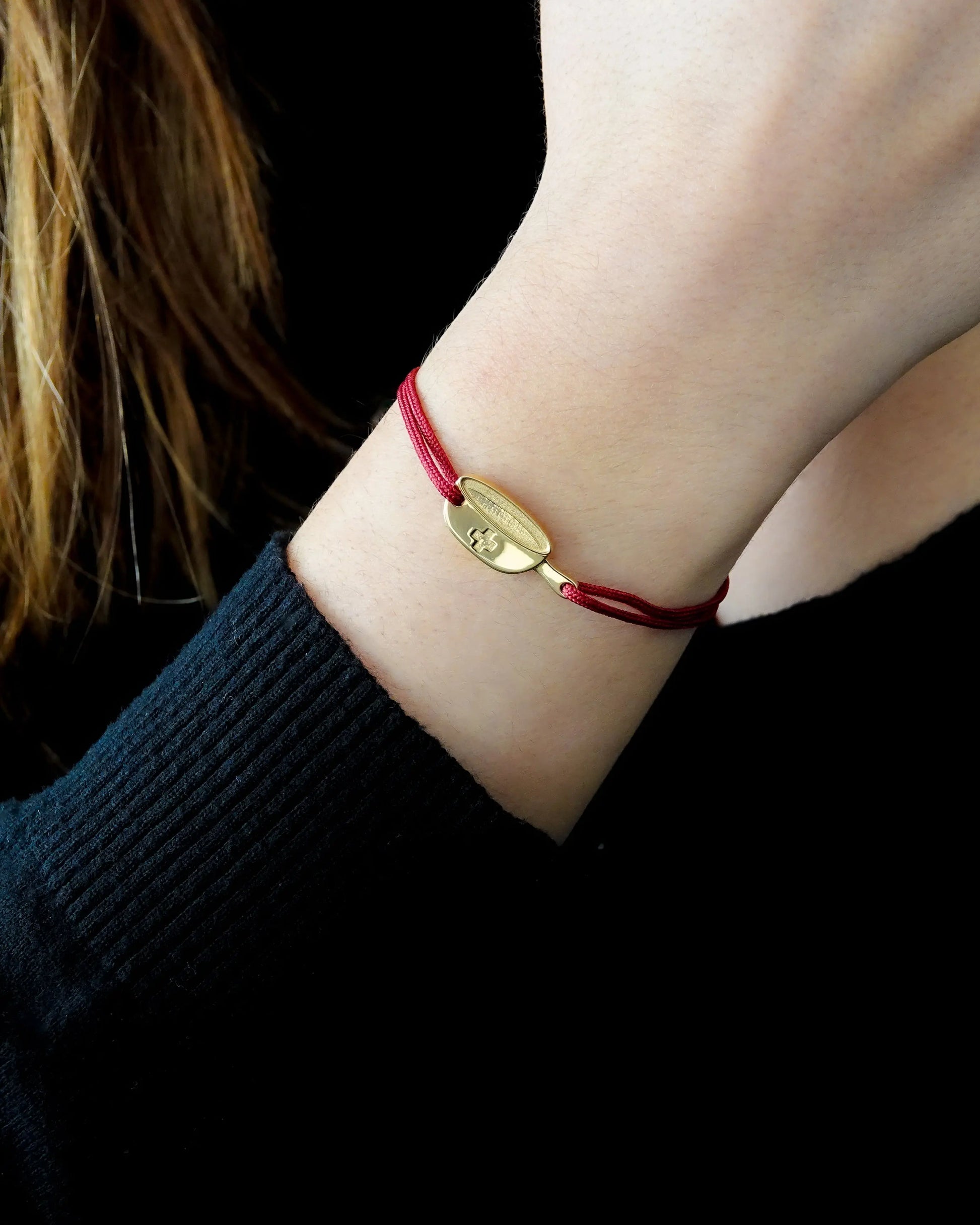 Bracelet SwissFondue en argent plaqué or jaune et cordon rouge sur un poignet de femme