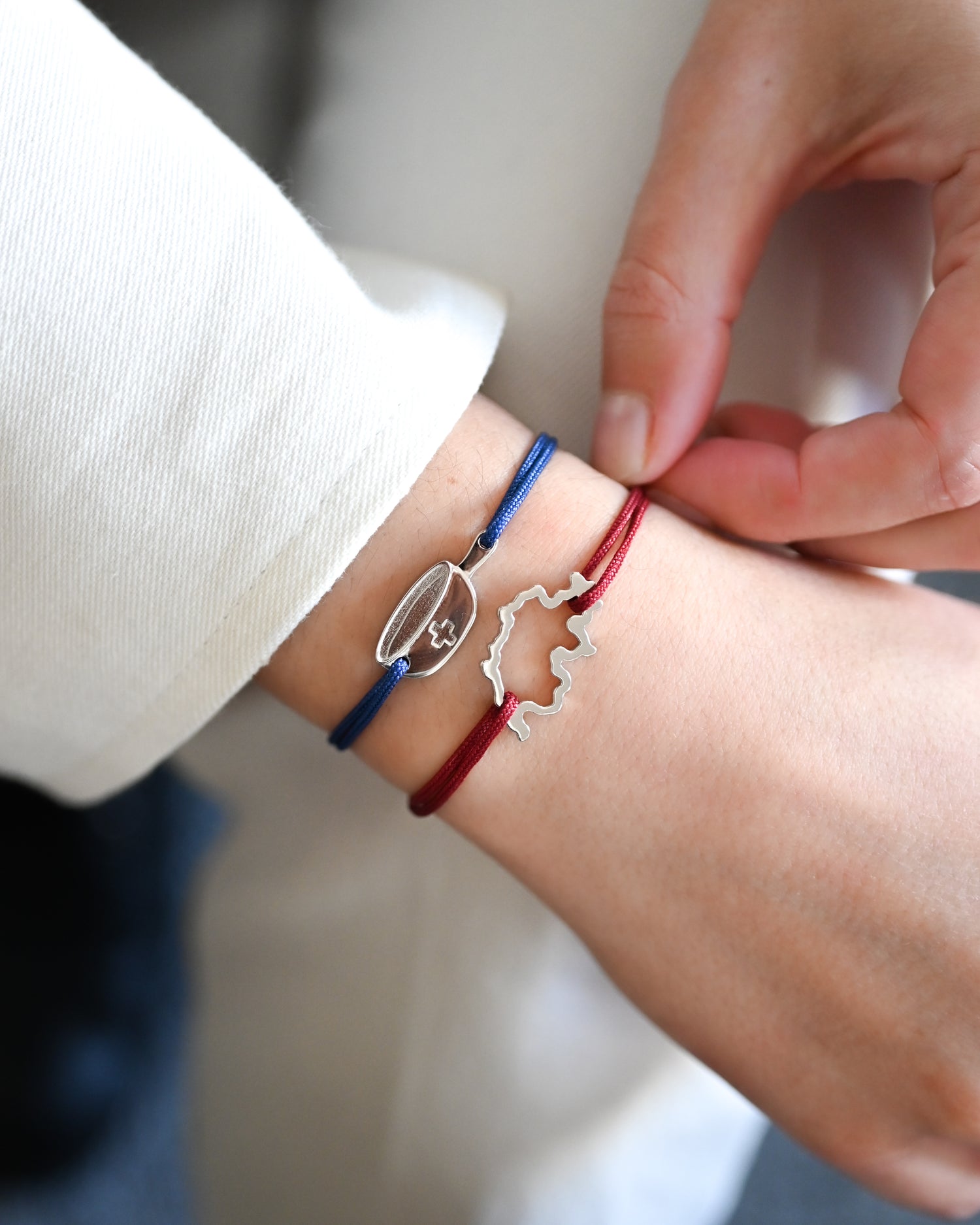 Bracelet SwissFondue en argent rhodié et cordon bleu et bracelet SwissMap en argent rhodié et cordon rouge sur un poignet de femme