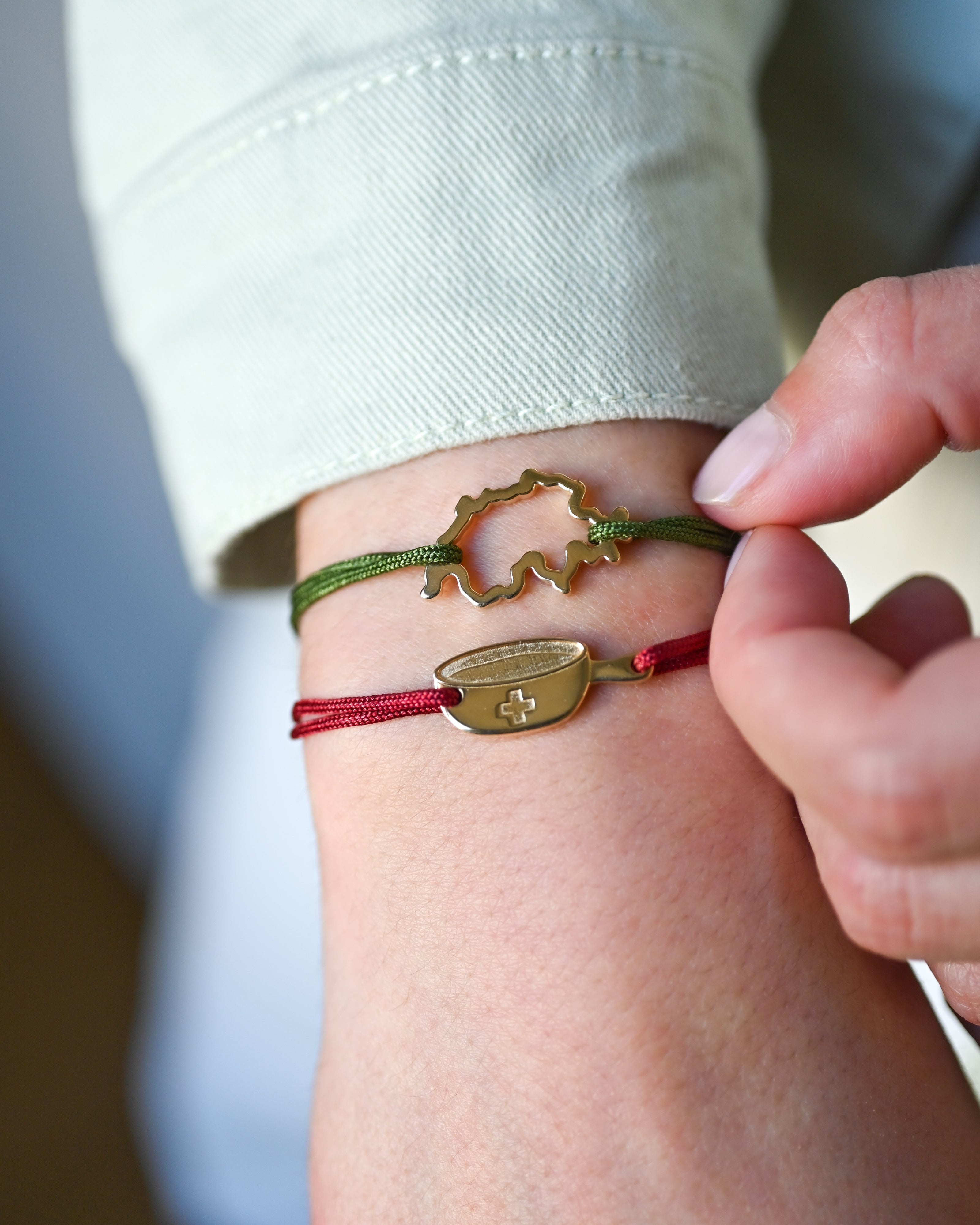 Bracelet SwissMap en argent plaqué or jaune et cordon vert et bracelet SwissFondue en argent plaqué or jaune et cordon rouge sur un poignet de femme
